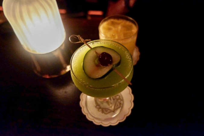 Up close of a cocktail decorated with a cucumber and cherry, on a candlelit table
